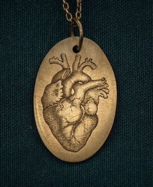 Gold oval pendant with an engraved, life-like, heart in the center.