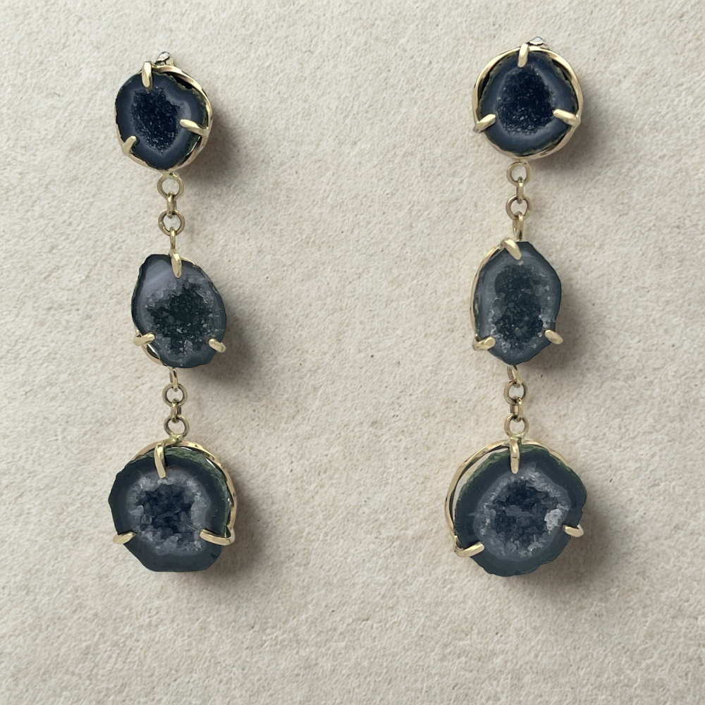 Gold dangle drop earrings. Each earring has three blue geodes, hanging straight down from each other. Each geode is set into a three prong gold setting.