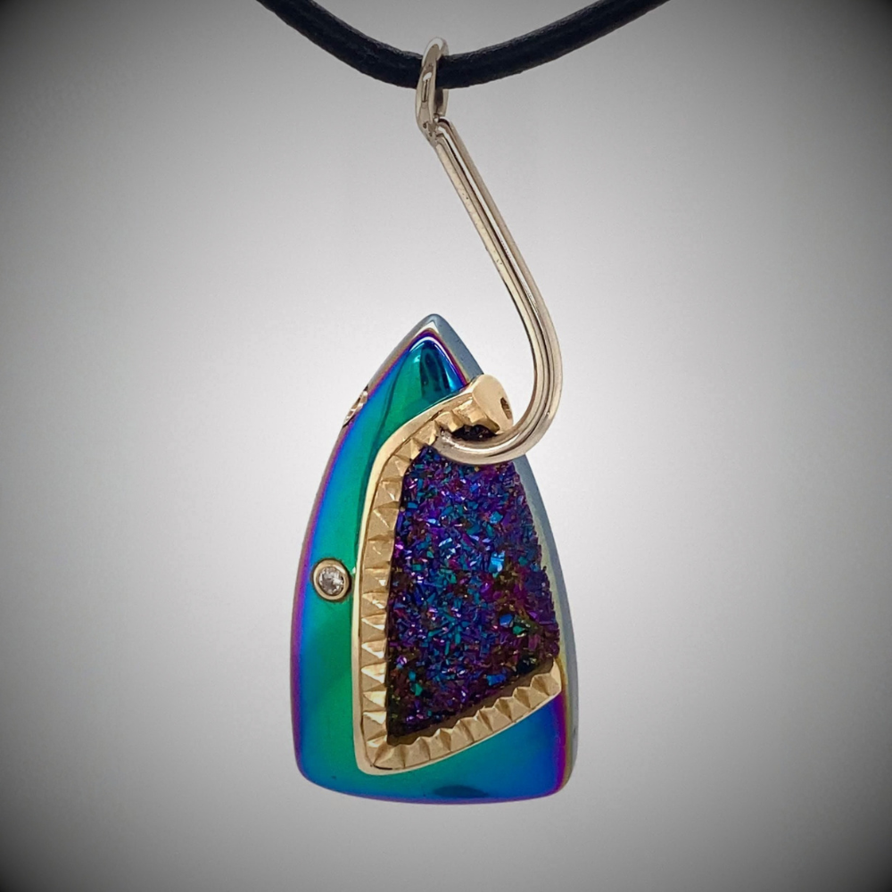 Rainbow metallic shark pendant, with gold teeth and a gold hook in its mouth. The eye is a diamond set in a gold bezel. Inside the sharks mouth is a metallic rainbow geode.